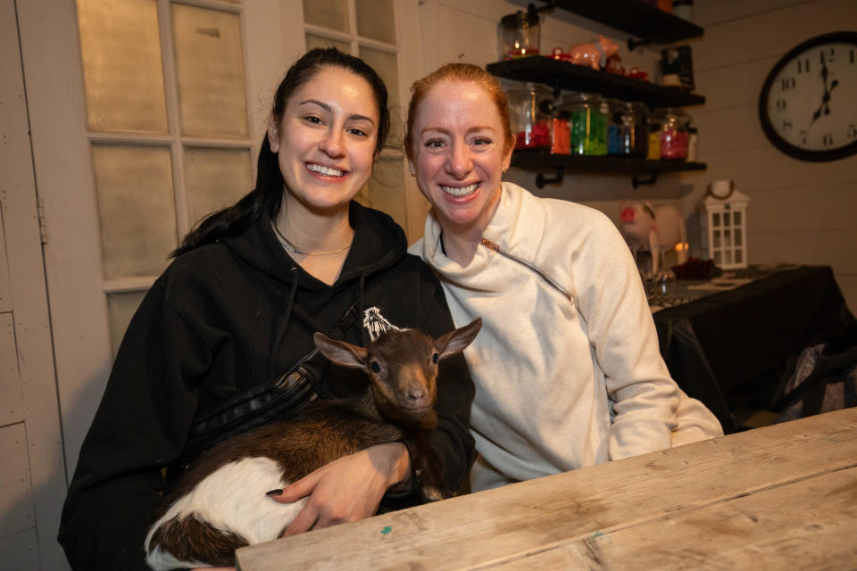Mikayla Harvey of Colorado and Becky McClelland of Salem pose for a photo while holding a baby goat at Wine-yasa Goat Yoga night at Legacy Lane Farm in Stratham.