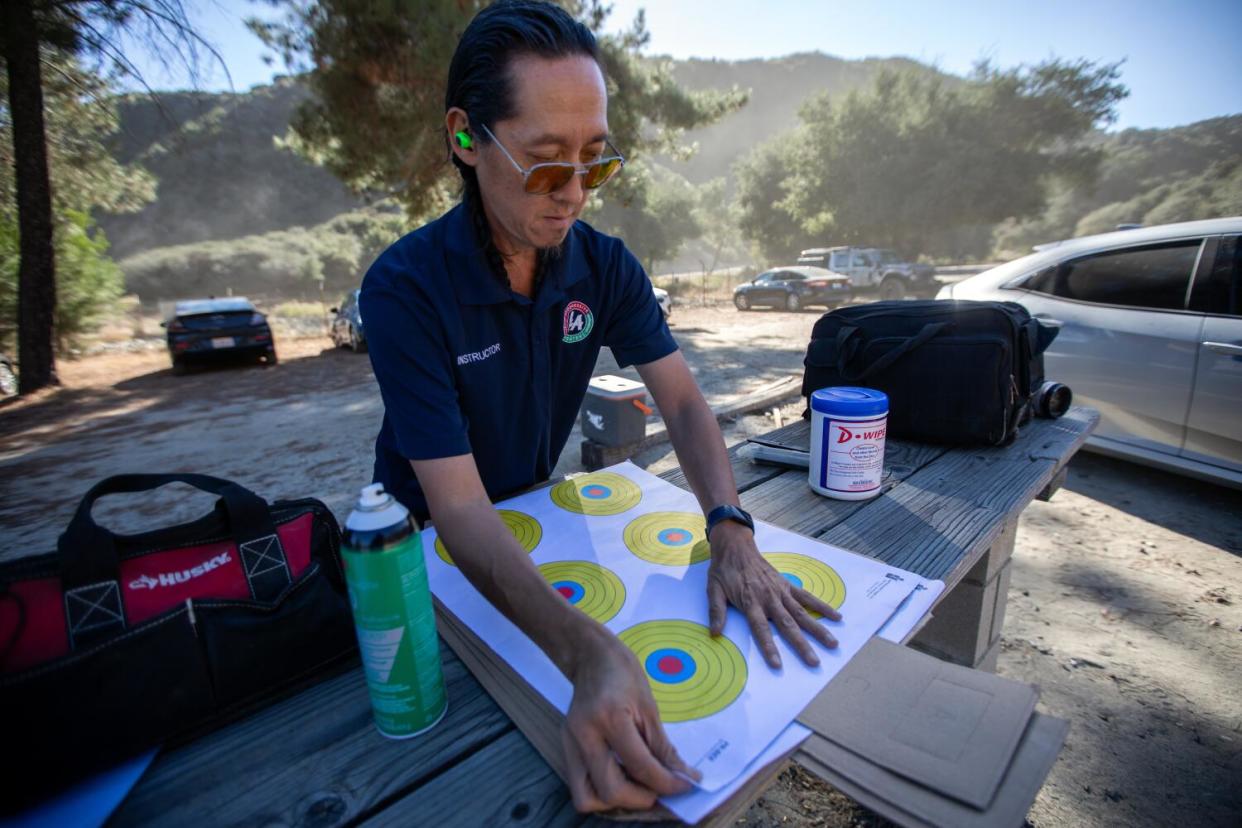 Tom Nguyen wearing ear plugs and aviator sunglasses as he prepares paper shooting targets at a table in a canyon