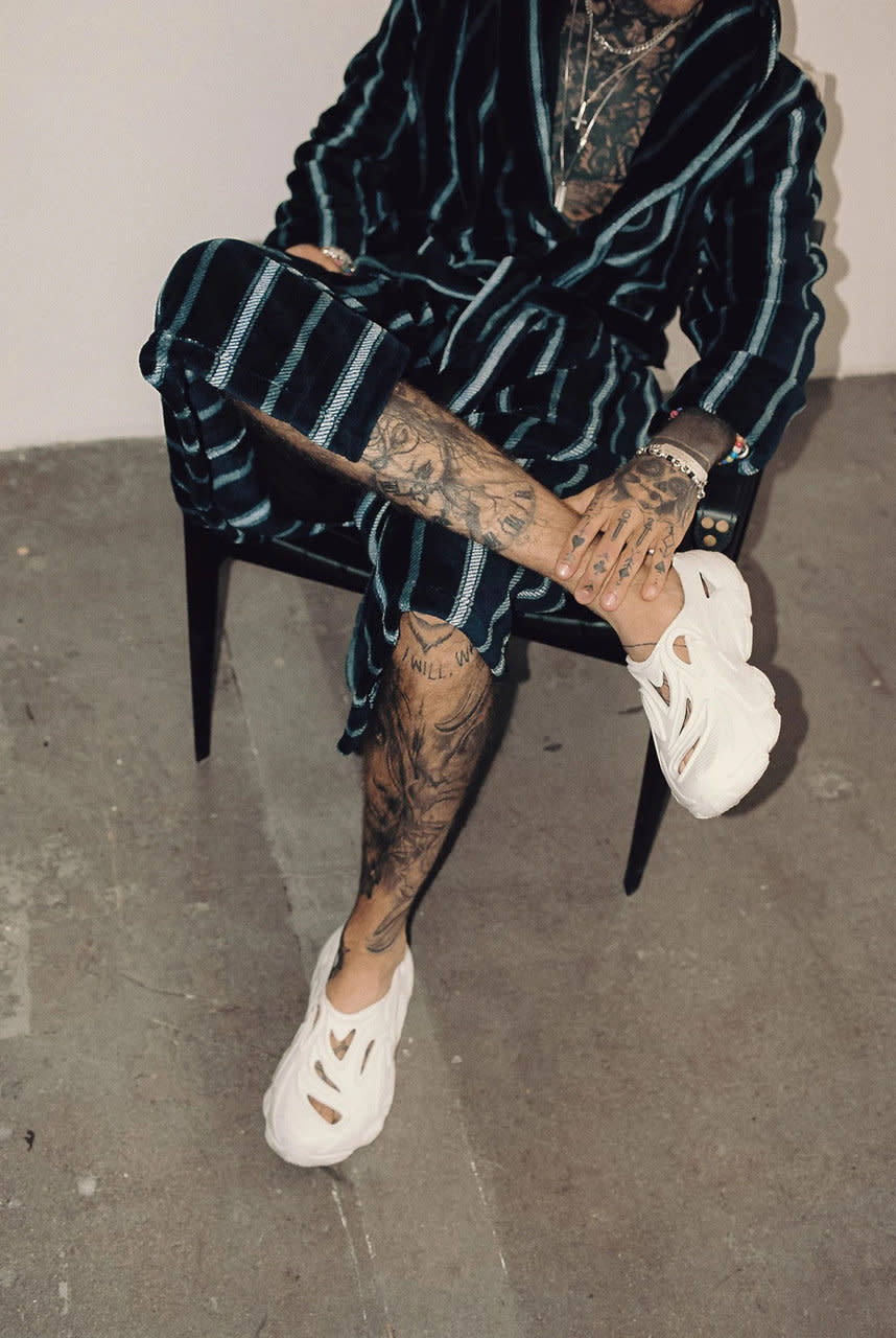 Man sits in a chair while showing off his upcycled Plastic Soul sneakers.