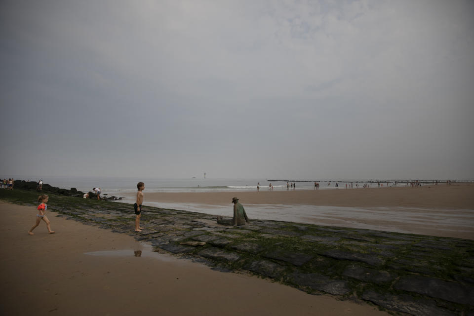 Two children play next to a statue along the coastline at the Belgian seaside resort of Knokke, Belgium, Tuesday, Aug. 11, 2020. At the seaside resort of Knokke-Heist, where golf carts with license plates ply well-kept streets, there was ample room to stretch out on the local beach this week. Local authorities have banished day trippers from Belgian cities or France from its 15-kilometer (10-mile) stretch of sands until the heat wave is over. (AP Photo/Virginia Mayo)