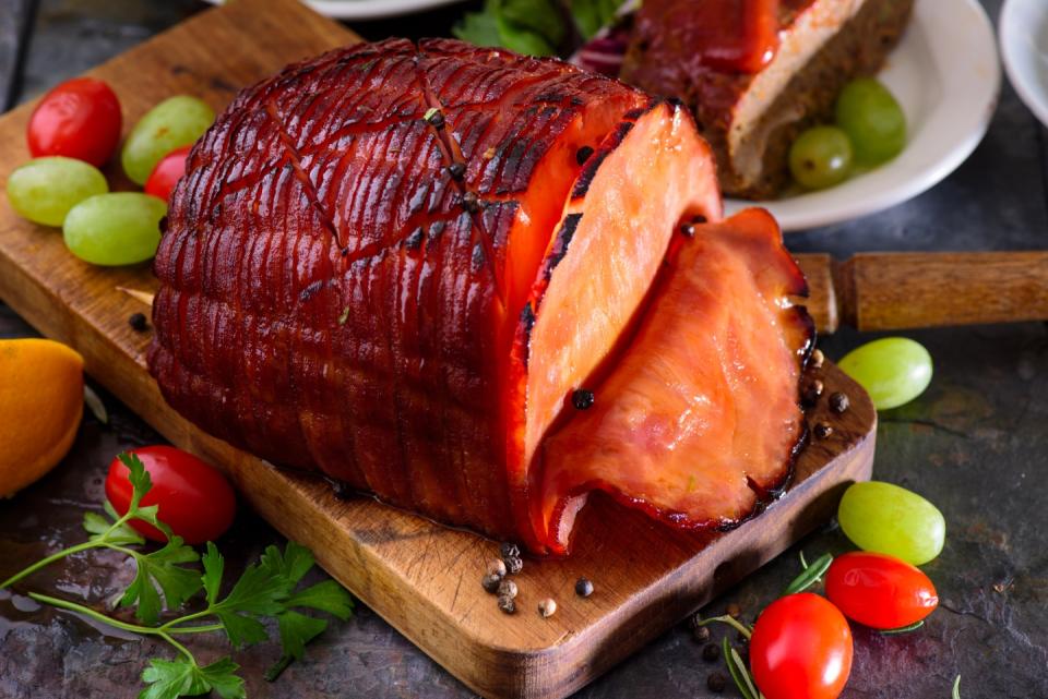 Holiday glazed sliced ham with green grapes and cherry tomatoes on dinner table. (Photo: Getty Images)