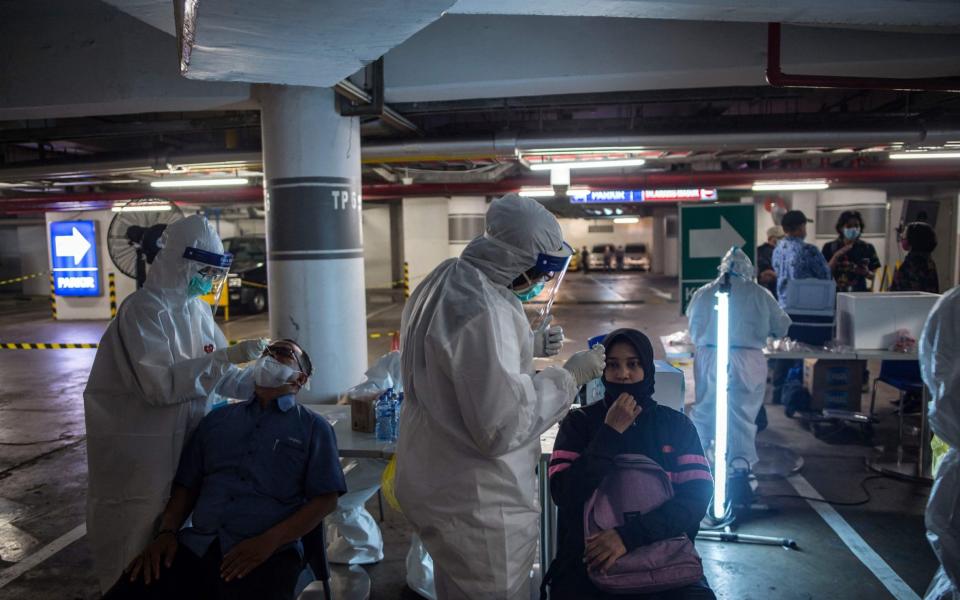 In Surabaya, Indonesia, health workers collect swab samples from shoppers to test for Covid-19 before they are allowed to enter a shopping mall - Juni Kriswanto / AFP