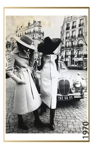 Two models posing on the streets of Paris, in large brimmed suede and felt hats, paired with a belted, wool, knee length coat and a vinyl, knee length, raincoat, over dark colored pants and shoes, from the Jay Jaxon Spring/ Summer 1970 collection for Maison Jean-Louis Scherrer, 1970.