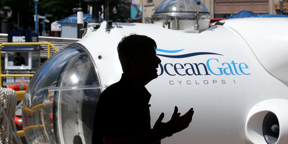 silhouette of man gesturing in front of white submersible with words oceangate on the side