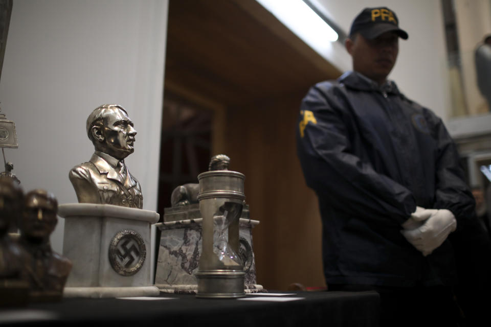 A police officer stands in front of a cache of Nazi artifacts discovered in 2017, during a press conference in Buenos Aires, Argentina, Wednesday, Oct. 2, 2019. Argentine authorities found the cache in a secret room behind a bookcase and had uncovered the collection in the course of a wider investigation into artwork of suspicious origin found at a gallery in Buenos Aires. (AP Photo/Natacha Pisarenko)