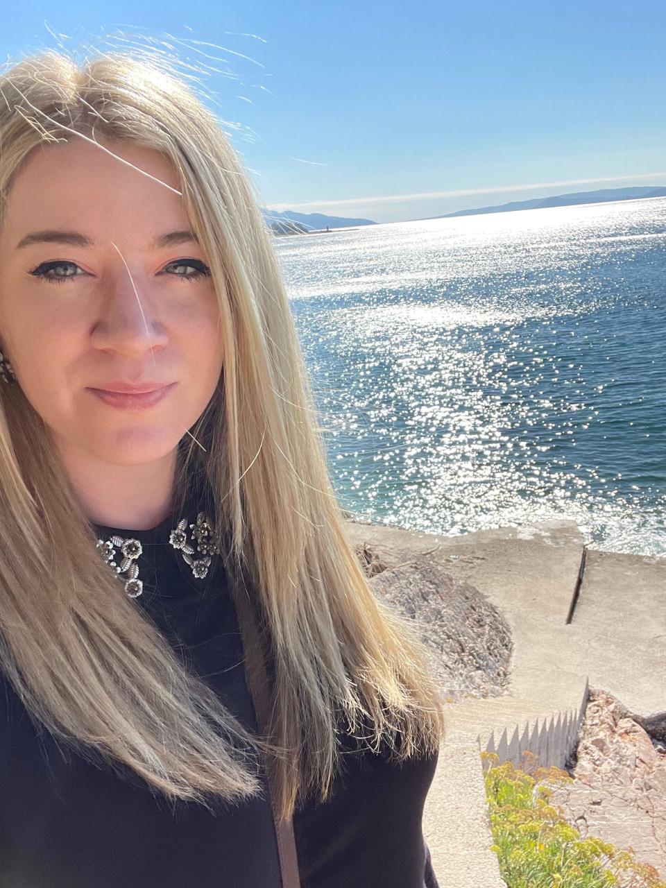 A blonde woman takes a selfie in front of the sea.