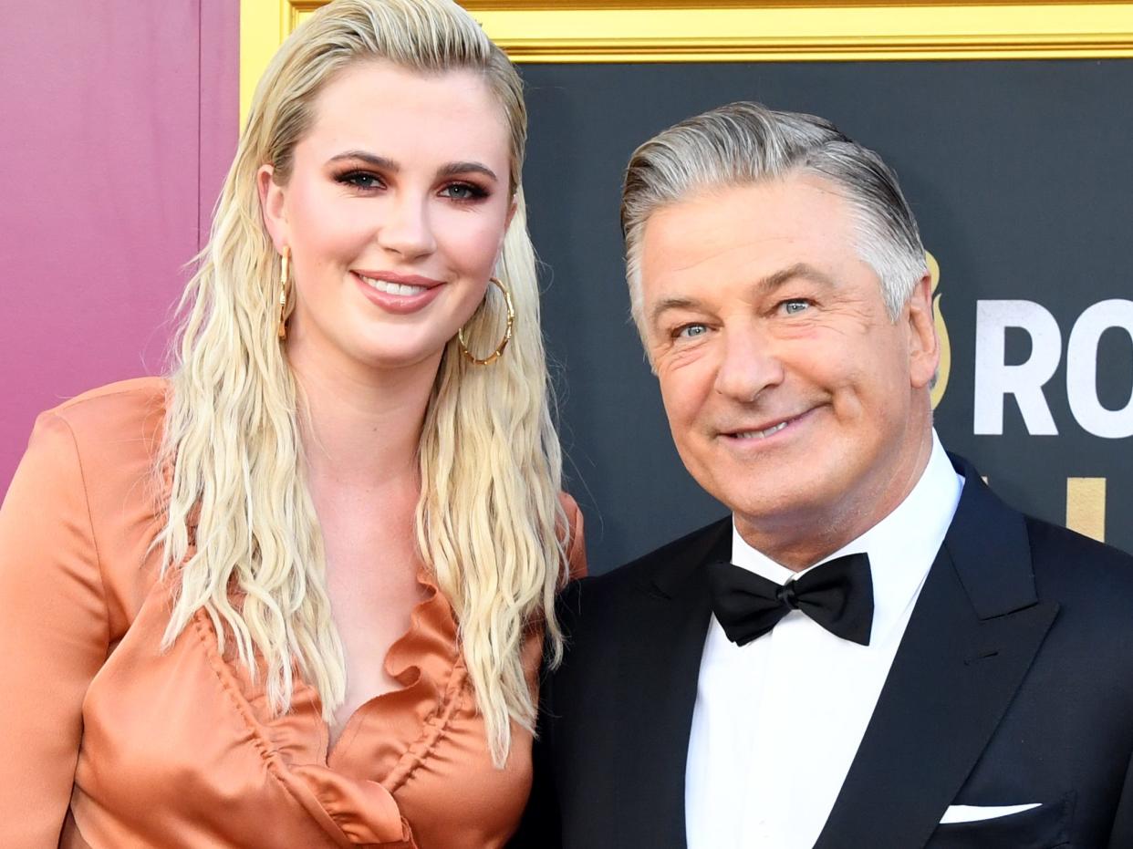 Ireland Baldwin wears an orange dress and Alec Baldwin wears a black suit and bowtie at a red carpet in September 2019.