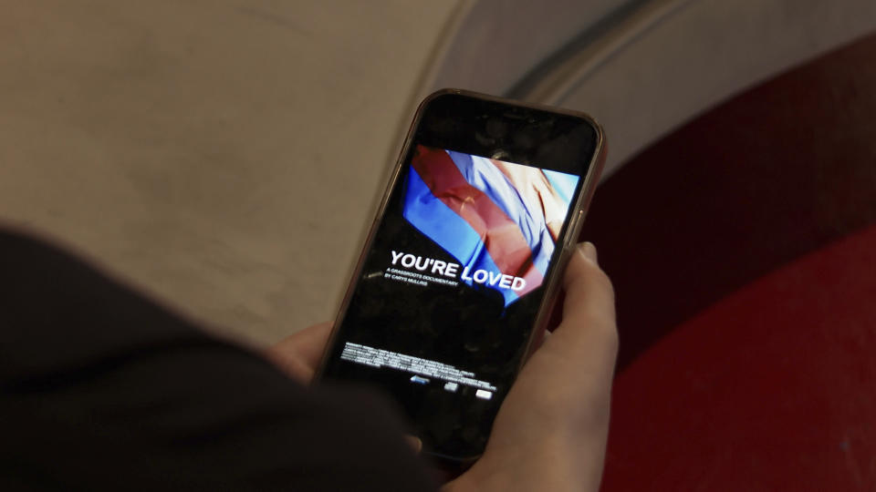 Carys Mullins looks at the poster for their documentary, “You’re Loved,” at Green Light Cinema in St. Petersburg, Fla. on March 27, 2023. The Florida teenager has documented how it feels to be young and transgender for a film set to debut at a festival as transgender people around the world celebrate visibility and lawmakers across the country look to restrict their rights and care. (AP Photo/Laura Bargfeld)