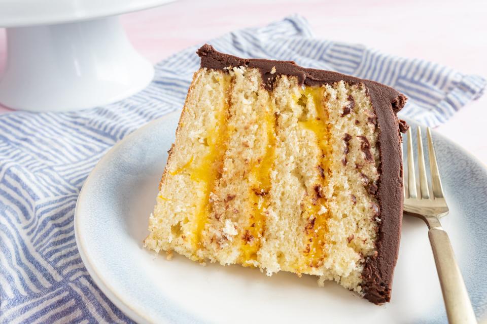 a slice of yellow cake with orange layers and chocolate frosting on a plate with a fork