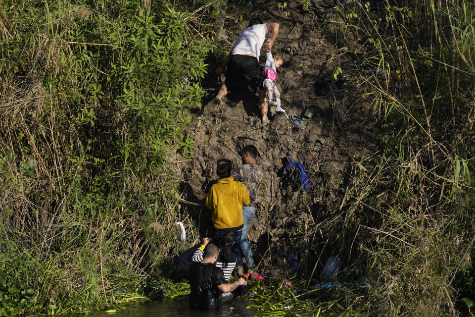 A Venezuelan migrant holds onto a child as he climbs a river bank onto U.S territory, after crossing a river from Matamoros, Mexico, Thursday, Dec. 22, 2022. (AP Photo/Fernando Llano)
