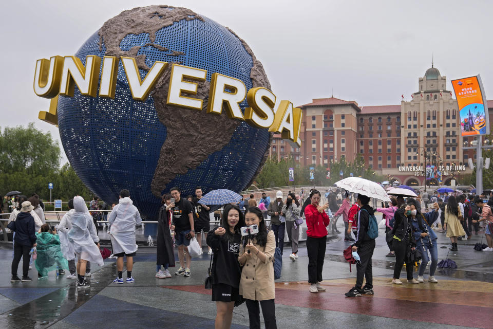 People take selfies with an icon near the entrance to Universal Studios Beijing in Beijing, Monday, Sept. 20, 2021. Thousands of people brave the rain visit to the newest location of the global brand of theme parks which officially opens on Monday. (AP Photo/Andy Wong)