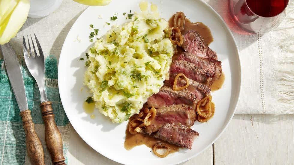 strip steak with lemon mashed potatoes on a white plate with silverware and a glass of wine