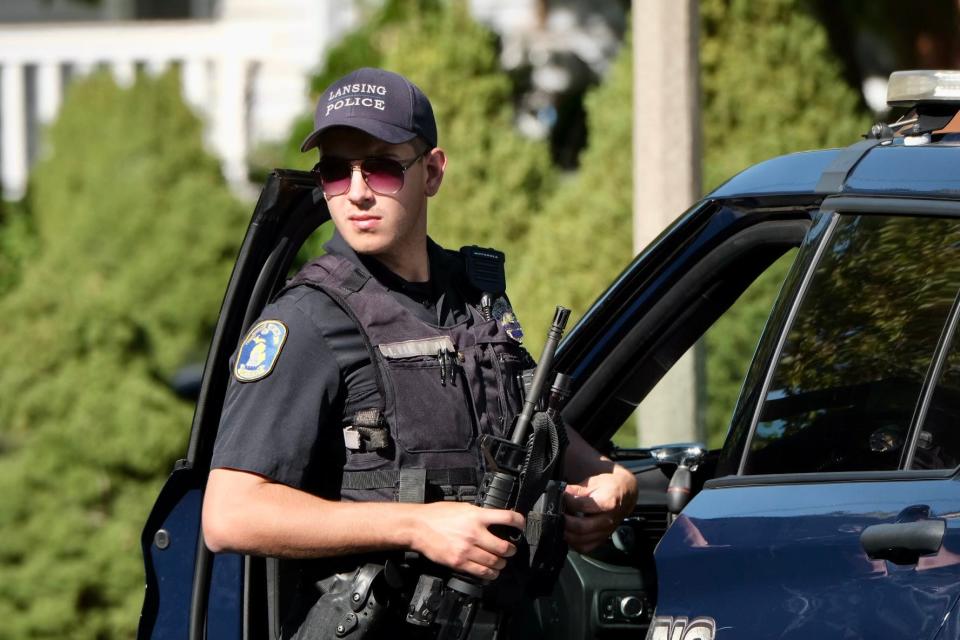 A Lansing Police Department officer secures his weapon at the scene of a double shooting on Riddle Street in Lansing.