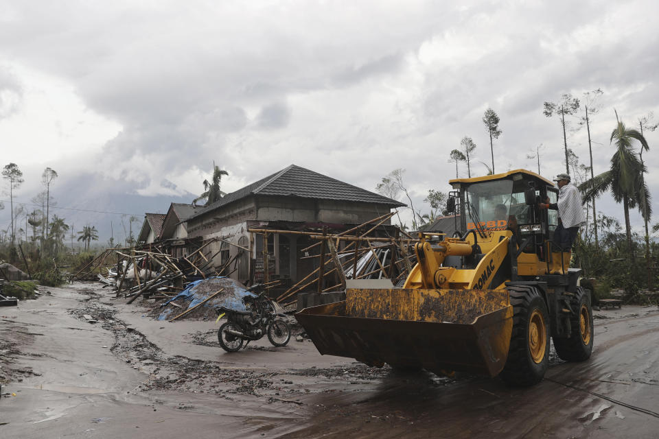 Workers clean debris following an eruption of Mount Semeru, seen in the background, in Lumajang district, East Java province, Indonesia, Monday, Dec. 6, 2021. The highest volcano on Java island spewed thick columns of ash into the sky in a sudden eruption Saturday triggered by heavy rains. Villages and nearby towns were blanketed and several hamlets buried under tons of mud from volcanic debris. (AP Photo/Trisnadi)