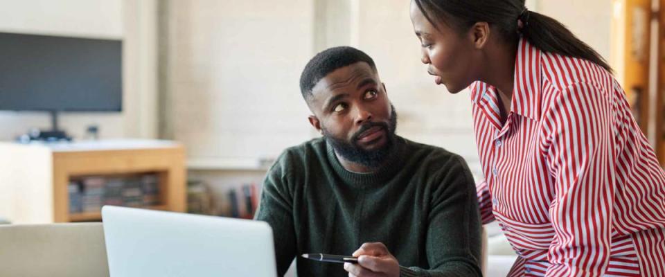 Young African American couple paying bills online with a laptop at their dining room table at home