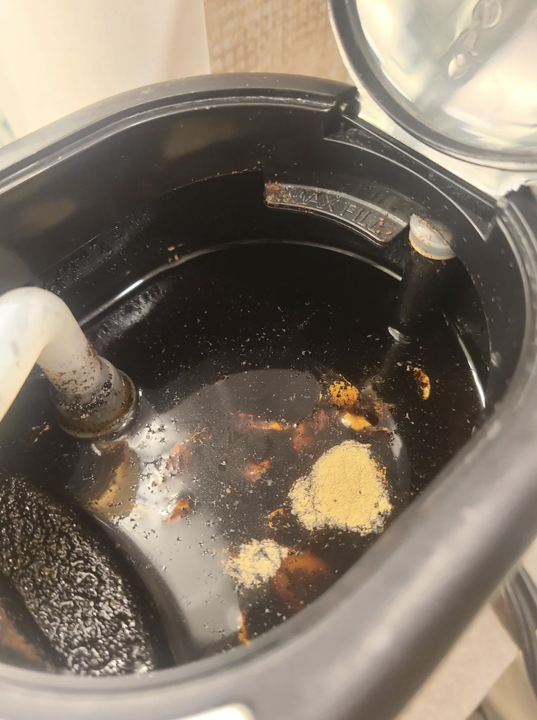 Inside of a coffee-maker with residue and stagnant-looking liquid and grinds