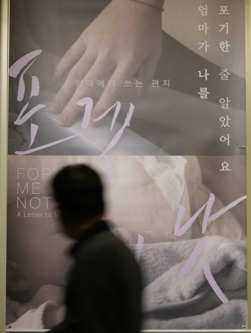 A visitor walks past a poster of film "Forget Me Not," at a movie theater in Seoul, South Korea on June 4, 2021. The shock and grief of mother-child separations and intense fear of social stigma captured in “Forget Me Not” offer insight into what’s possibly preventing the Danish filmmaker and thousands of other Korean adoptees from reconnecting with their silenced birth mothers, decades after they were jetted to the West. (AP Photo/Lee Jin-man)