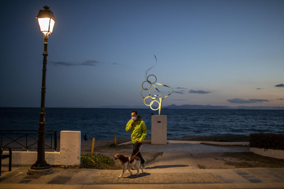 A man wearing a protective face mask walks with is dog in Alimos, a seaside suburb of Athens, on Tuesday, April 20, 2021. (AP Photo/Petros Giannakouris)