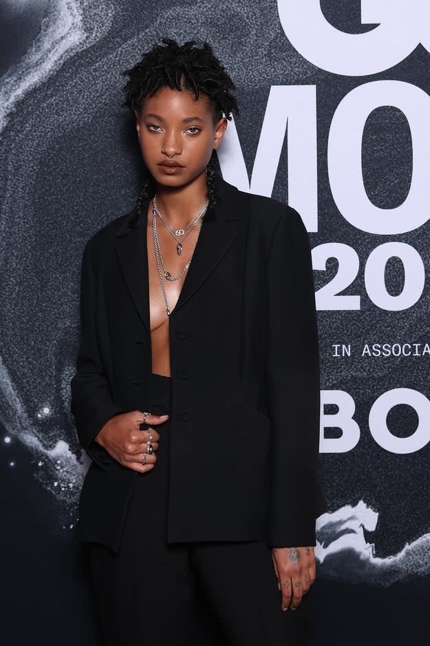 Willow Smith wears a black blazer over a bare chest with necklaces, posing on the red carpet