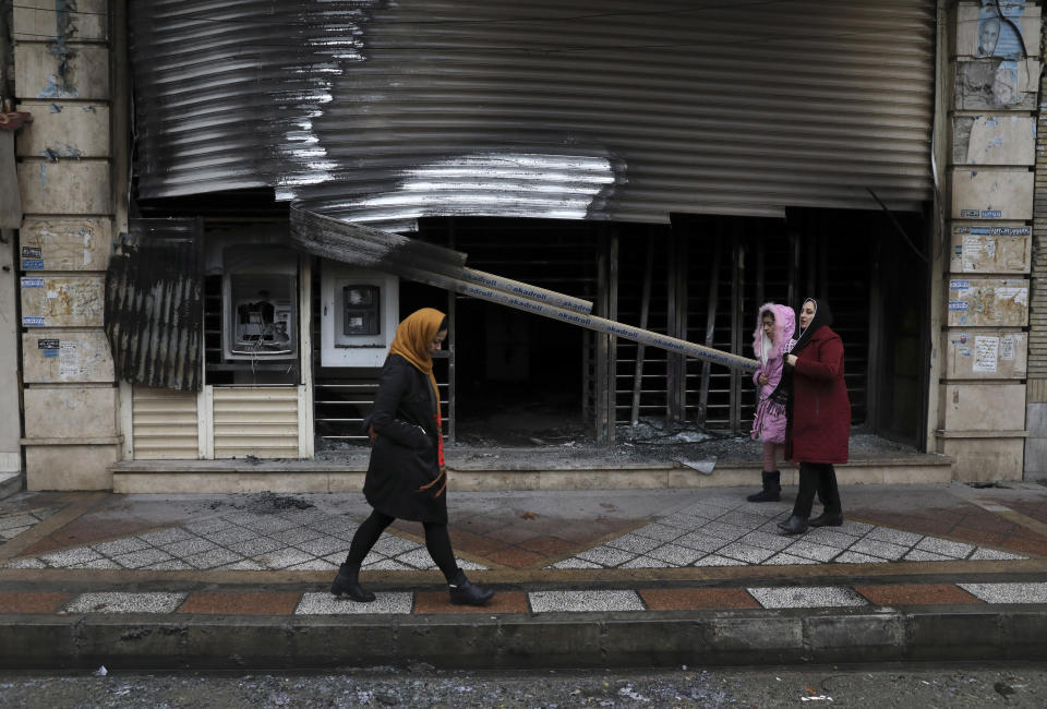 People walk past a bank that was burned during recent protests, in Shahriar, Iran, some 40 kilometers (25 miles) southwest of the capital, Tehran, Wednesday, Nov. 20, 2019. Protests over government-set gasoline prices rising struck at least 100 cities and towns, spiraling into violence that saw banks, stores and police stations attacked and burned. (AP Photo/Vahid Salemi)