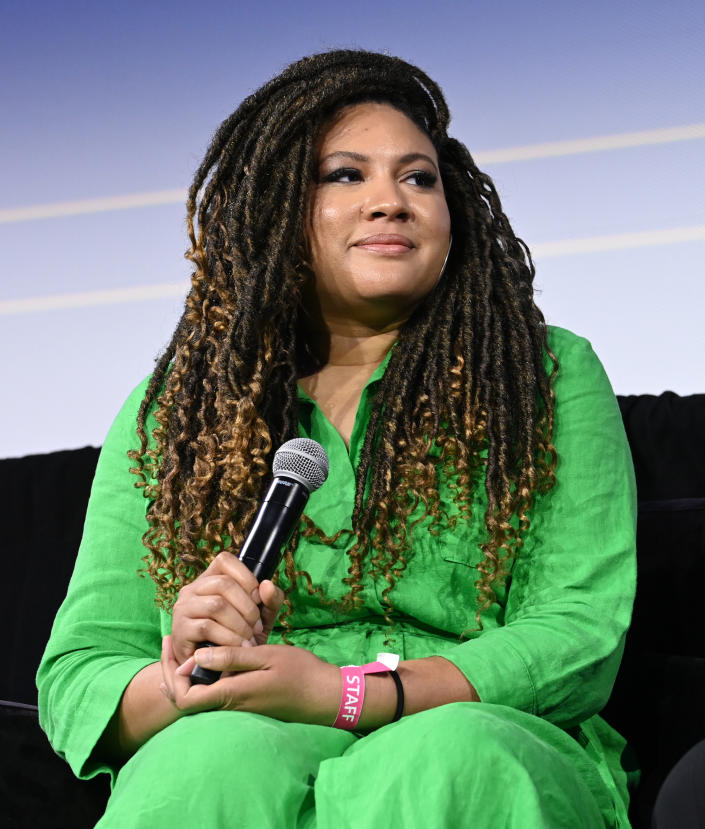 Tracy Oliver wearing a green outfit and holding a microphone. 