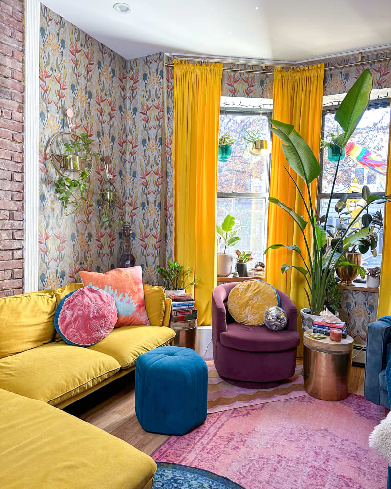Living room with colorful patterned wallpaper, yellow curtains and sofa, and some exposed brick