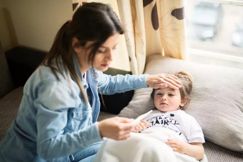 Mother checking temperature on sick daughter laying in bed