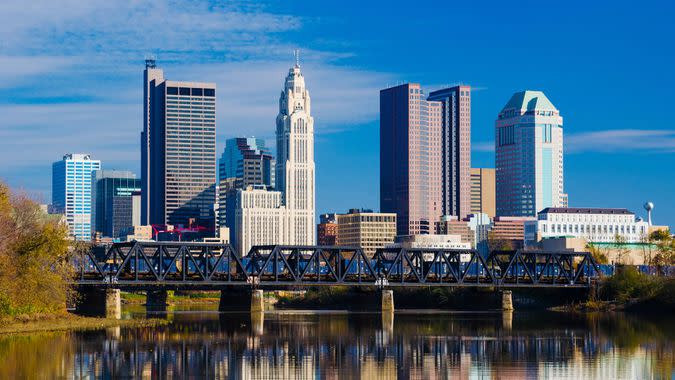 Downtown Columbus skyline, a train bridge, and the Scioto River with skyline reflection in the foreground.