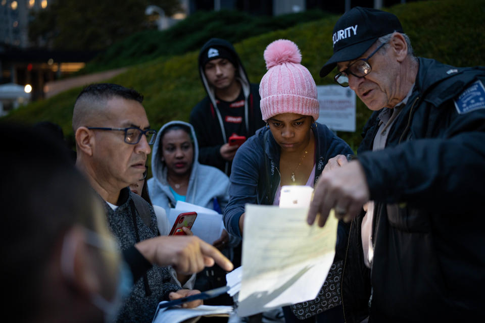 Un guardia de seguridad ayuda a los migrantes que esperan para solicitar asilo a entender la documentación, afuera de un tribunal federal en Manhattan, el 26 de octubre de 2022. (Mostafa Bassim/The New York Times)