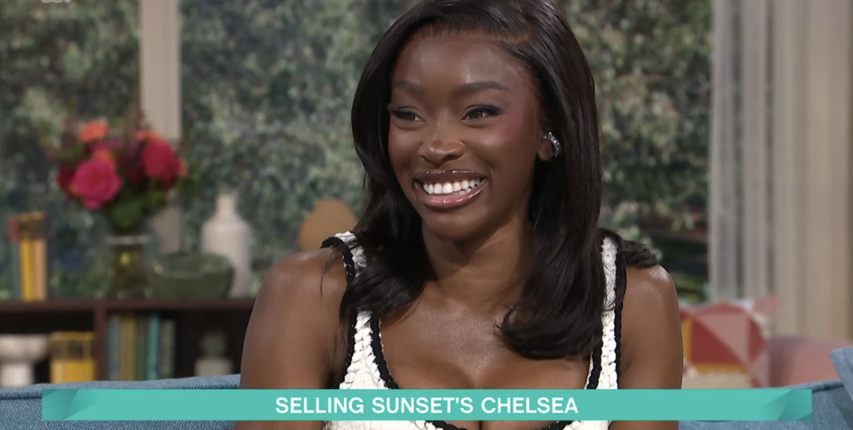 Chelsea Lazkani from Selling Sunset smiles brightly during an interview wearing a chic sleeveless dress with a white lace accent