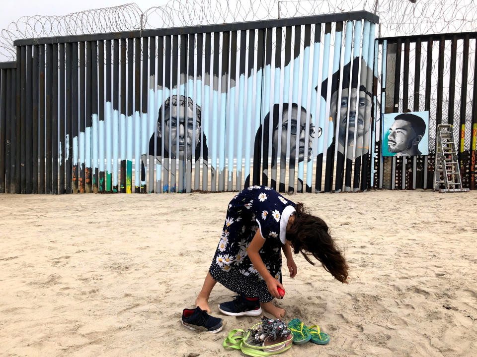 A girl stands near a new mural which has been painted on the Mexican side of a border wall in Tijuana, Mexico, Friday, Aug. 9, 2019. The mural shows faces of people deported from the U.S. with barcodes that activate first-person narratives on visitors' phones. Lizbeth De La Cruz Santana conceived the interactive mural in Tijuana as part of doctoral dissertation at the University of California, Davis. (AP Photo/Elliot Spagat)