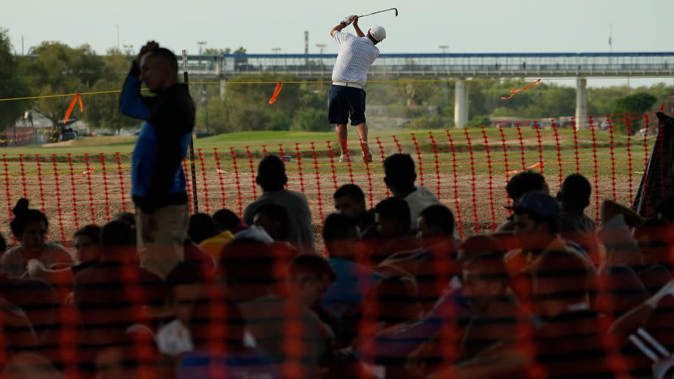 Migrants who crossed into the US from Mexico watch a golfer from a makeshift processing area along the Rio Grande, on Thursday, Sept. 21, 2023, in Eagle Pass, Texas. - Eric Gay/AP