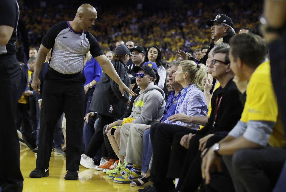 In this photo taken Wednesday, June 5, 2019, referee Marc Davis, left, gestures toward Golden State Warriors investor Mark Stevens, partially obscured in blue shirt, during the second half of Game 3 of basketball's NBA Finals between the Warriors and the Toronto Raptors in Oakland, Calif. An NBA spokesman said Thursday the conduct of Stevens at Game 3 of the NBA Finals was "beyond unacceptable." NBA Executive Vice President for Communications Mike Bass says that Stevens will not be permitted to attend games until the review of the matter is complete. The Warriors had already said he wouldn't be attending any more games in this series. (AP Photo/Ben Margot)