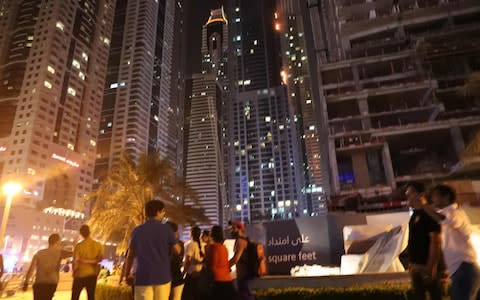 Bystanders look on as fire is seen at the 1,105 foot tall Torch tower skyscraper - Credit: AFP