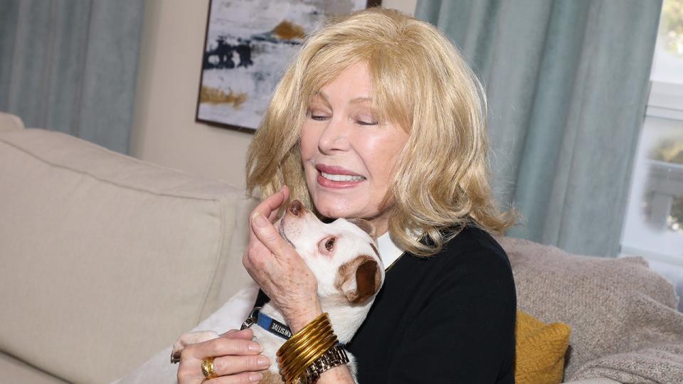 Loretta Swit smiling with her eyes closed as she embraces a small dog