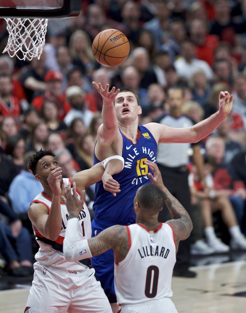 Denver Nuggets center Nikola Jokic, top, reaches for a rebound over Portland Trail Blazers guard Evan Turner, left, and guard Damian Lillard during the first half of Game 3 of an NBA basketball second-round playoff series Friday, May 3, 2019, in Portland, Ore. (AP Photo/Craig Mitchelldyer)