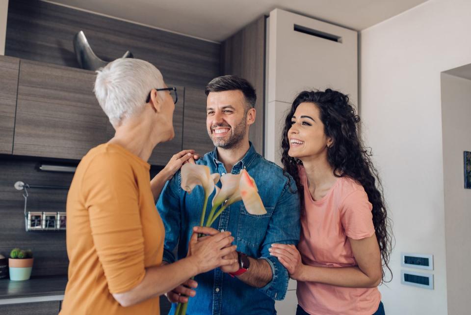 senior woman getting a flower bouquet from her son and daughter in law