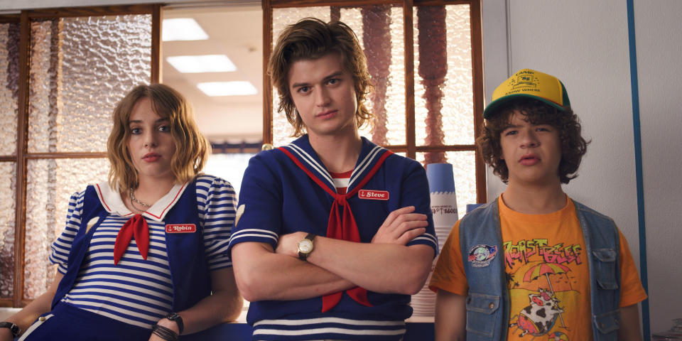 Robin and Steve (with arms crossed) in sailor outfits, and Dustin in a cap