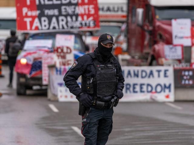 An Ottawa police officer stands near a row of protest vehicles and signs on Feb. 11, 2022.  (Jean-Francois Benoit/CBC - image credit)