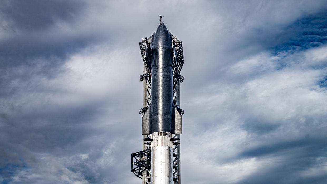  A black spacecraft stands atop its first stage booster on the launch pad with cloudy skies in the background. 