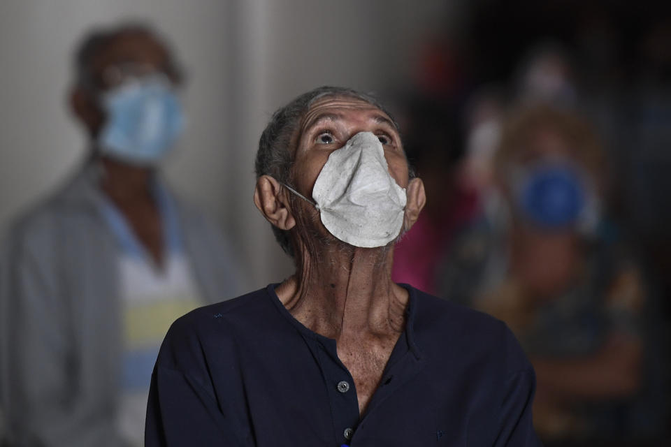 An elderly man, wearing a protective face mask as a precaution against the spread of the new coronavirus, prays during mass at a church in Caracas, Venezuela, Sunday, March 29, 2020. COVID-19 causes mild or moderate symptoms for most people, but for some, especially older adults and people with existing health problems, it can cause more severe illness or death. (AP Photo/Matias Delacroix)