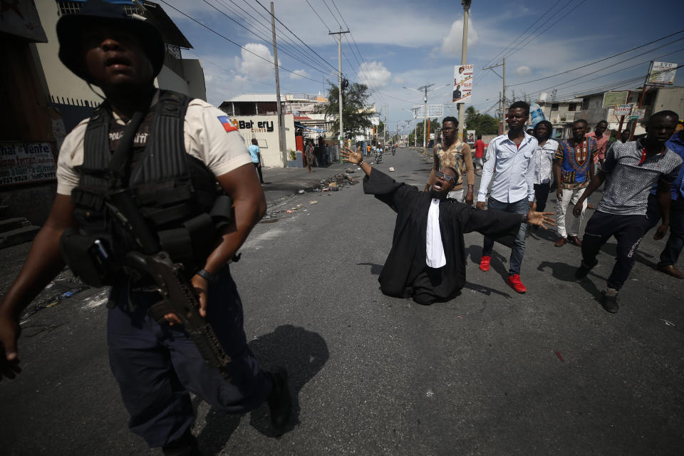 Paseus Juvensky St. Fleur, who trained as a lawyer and is now an activist working for social justice, drops to his knees as protestors trying to set up a barricade across a major road argue with police trying to stop them, in Port-au-Prince, Haiti, Wednesday, Oct. 2, 2019. A group of men was protesting at the intersection after commissioning a mural of opposition organizer Jose Mano Victorieux, known as "Badou," who they said was executed Saturday night by unknown assailants.(AP Photo/Rebecca Blackwell)