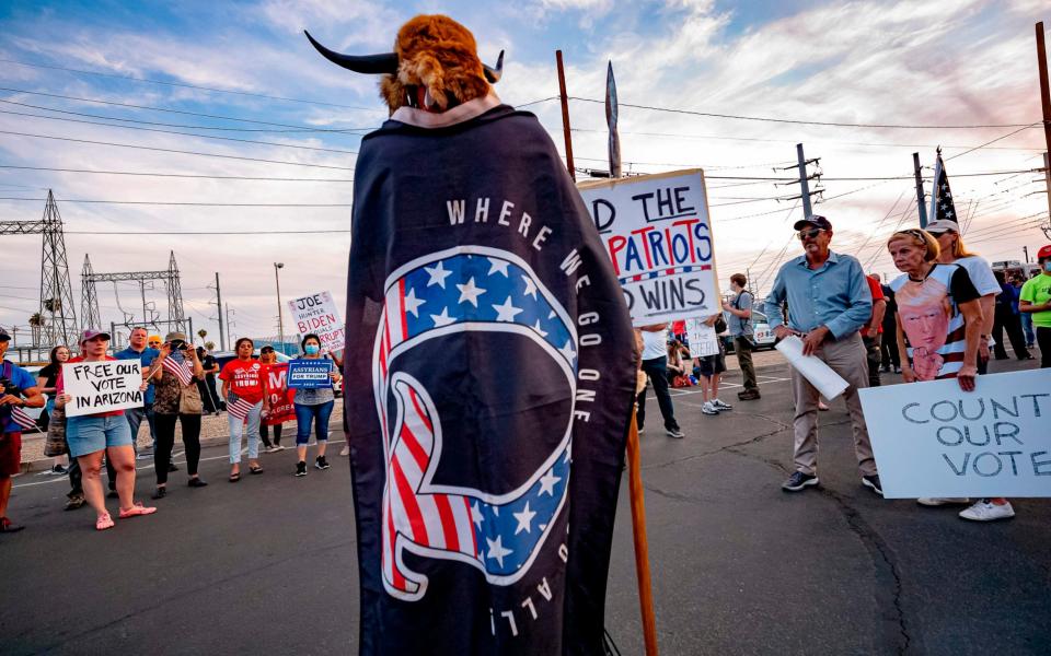 Jake Angeli, 33, aka Yellowstone Wolf, from Phoenix, wrapped in a QAnon flag, addresses supporters of US President Donald Trump as they protest outside the Maricopa County Election Department as counting continues after the US presidential election in Phoenix, Arizona, on November 5, 2020 - Olivier Touron/AFP