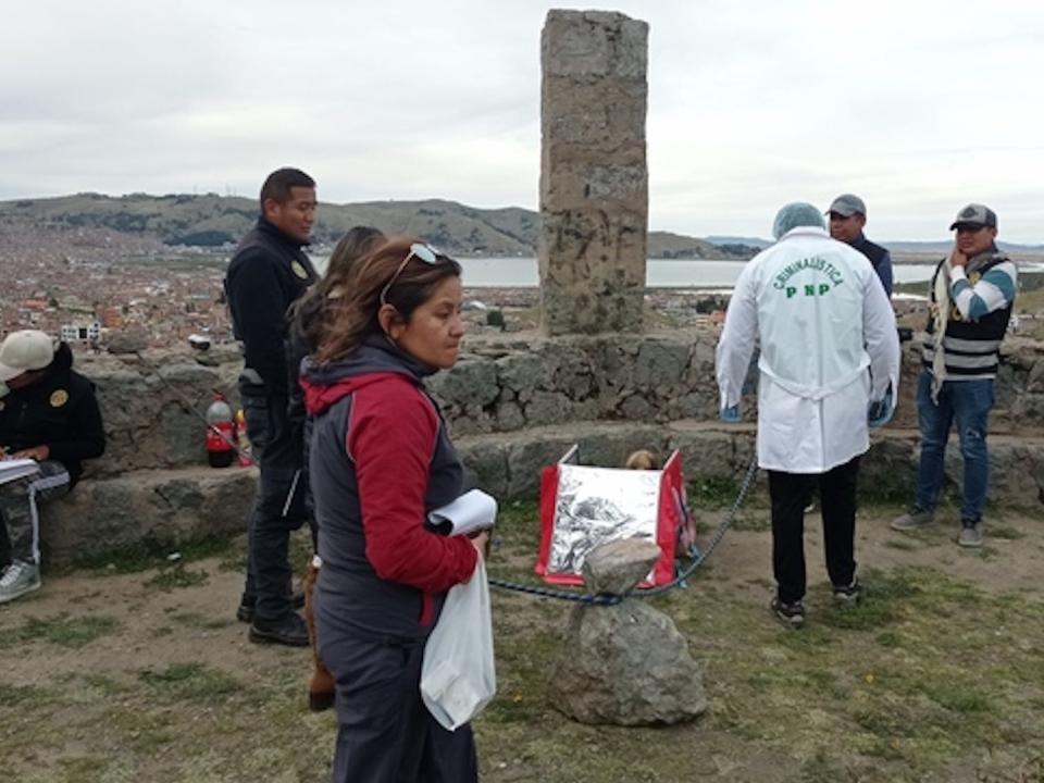 Authorities look at a delivery bag, empty, on the ground of an archeological site.