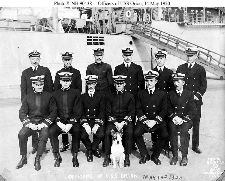 A black and white photo of officers of the USS Orion with the ship's dog