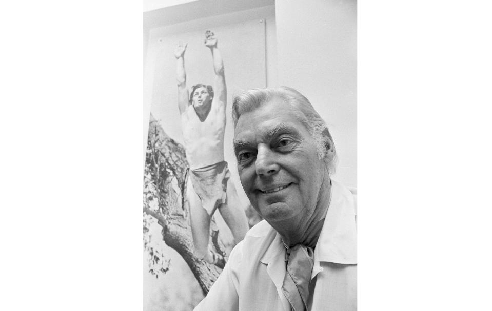 ARCHIVO - El héroe olímpico y actor de cine Johnny Weissmuller aparece frente a una fotografía de sí mismo como Tarzán, el 29 de junio de 1971. Weissmuller, quien interpretó a Tarzán en cine, fue una superestrella de la natación en Francia hace 100 años. (Foto AP, archivo)