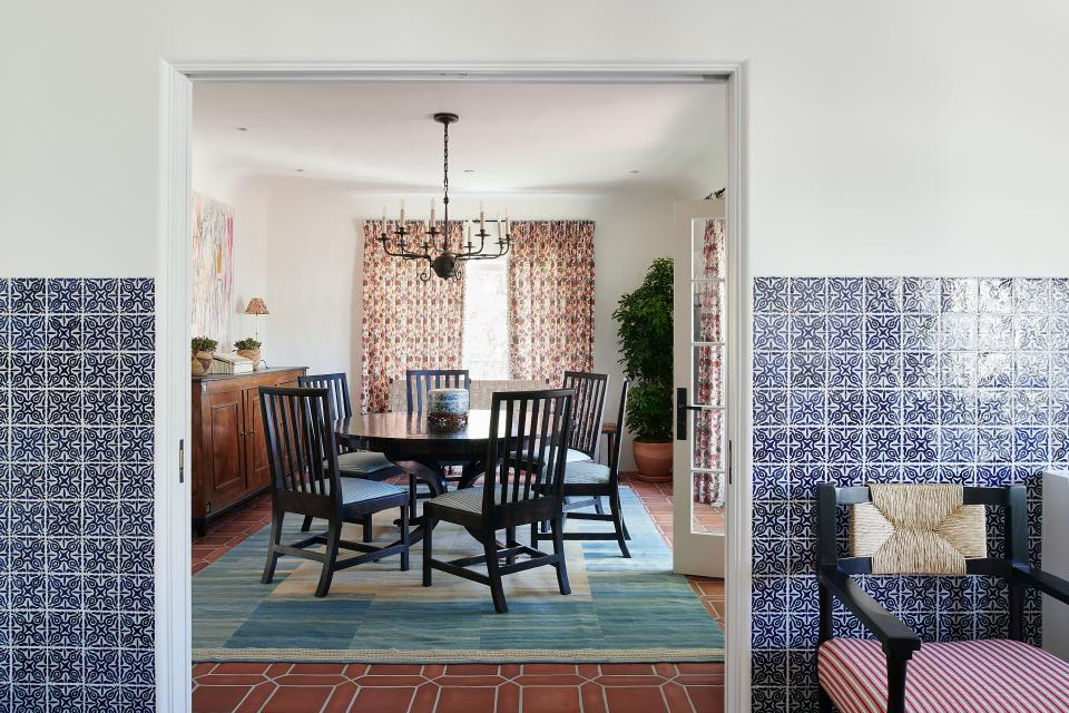 In the dining room, a Paul Ferrante chandelier hangs above a custom Dessin Fournir dining table surrounded by Century Furniture chairs embellished with Jennifer Shorto fabric; an Elizabeth Eakins rug anchors the arrangement. Quadrille drapery completes the space with a burst of vibrant pattern.