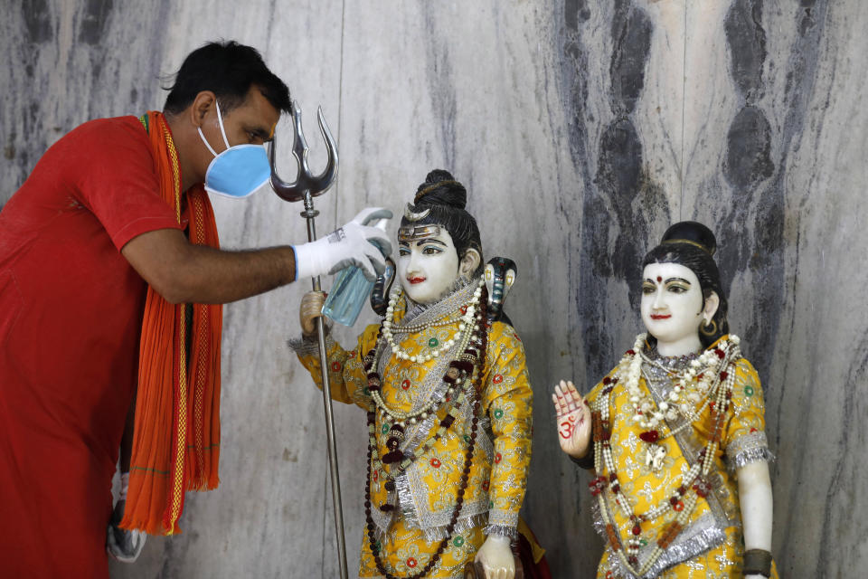 An Indian priest sanitizes the idol of Lord Shiva and Godess Parvati at a temple, in Prayagraj, India, Monday, June 8, 2020. Religious places, malls, hotels and restaurants open Monday after more than two months of lockdown as a precaution against coronavirus. (AP Photo/Rajesh Kumar Singh)