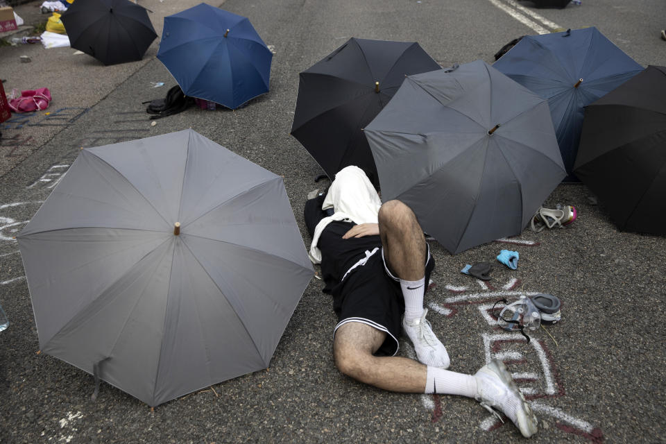 A pro-democracy protester takes a rest near umbrellas placed on a road outside the Chinese University campus in Hong Kong, Wednesday, Nov. 13, 2019. Police increased security around Hong Kong and its university campuses as they brace for more violence after sharp clashes overnight with anti-government protesters. (AP Photo/Ng Han Guan)