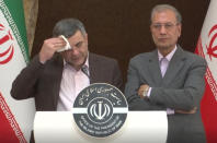 In this Monday Feb. 24, 2020 image made from video the head of Iran's counter-coronavirus task force, Iraj Harirchi, left, wipes his face during a press briefing with government spokesman Ali Rabiei, in Tehran, Iran. Harirchi, has tested positive for the virus himself, authorities announced Tuesday, amid concerns the outbreak may be far wider than officially acknowledged. The announcement regarding Harirchi came after the news conference seeking to minimize the danger posed by the outbreak. (APTN via AP)